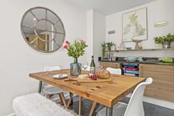 Modern dining room with wooden table, white chairs, a round mirror, and decorative shelves.