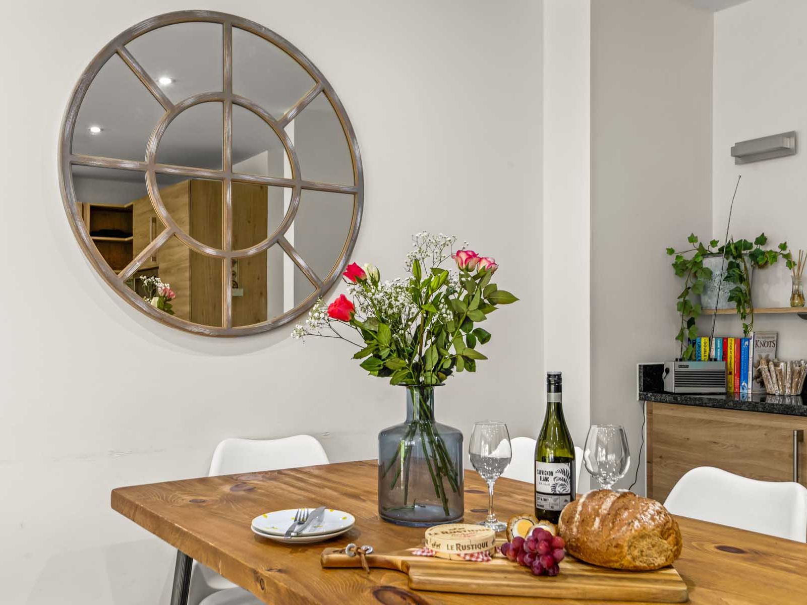 Dining table with flowers, bread, wine, and cheese in a modern kitchen with round decorative mirror