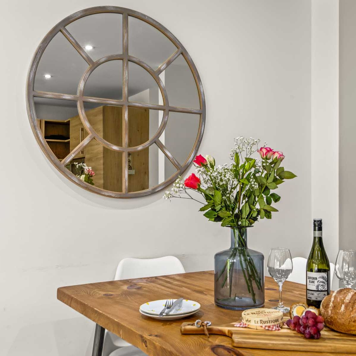 Dining table with flowers, bread, wine, and cheese in a modern kitchen with round decorative mirror