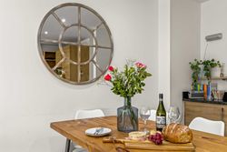 Dining table with flowers, bread, wine, and cheese in a modern kitchen with round decorative mirror