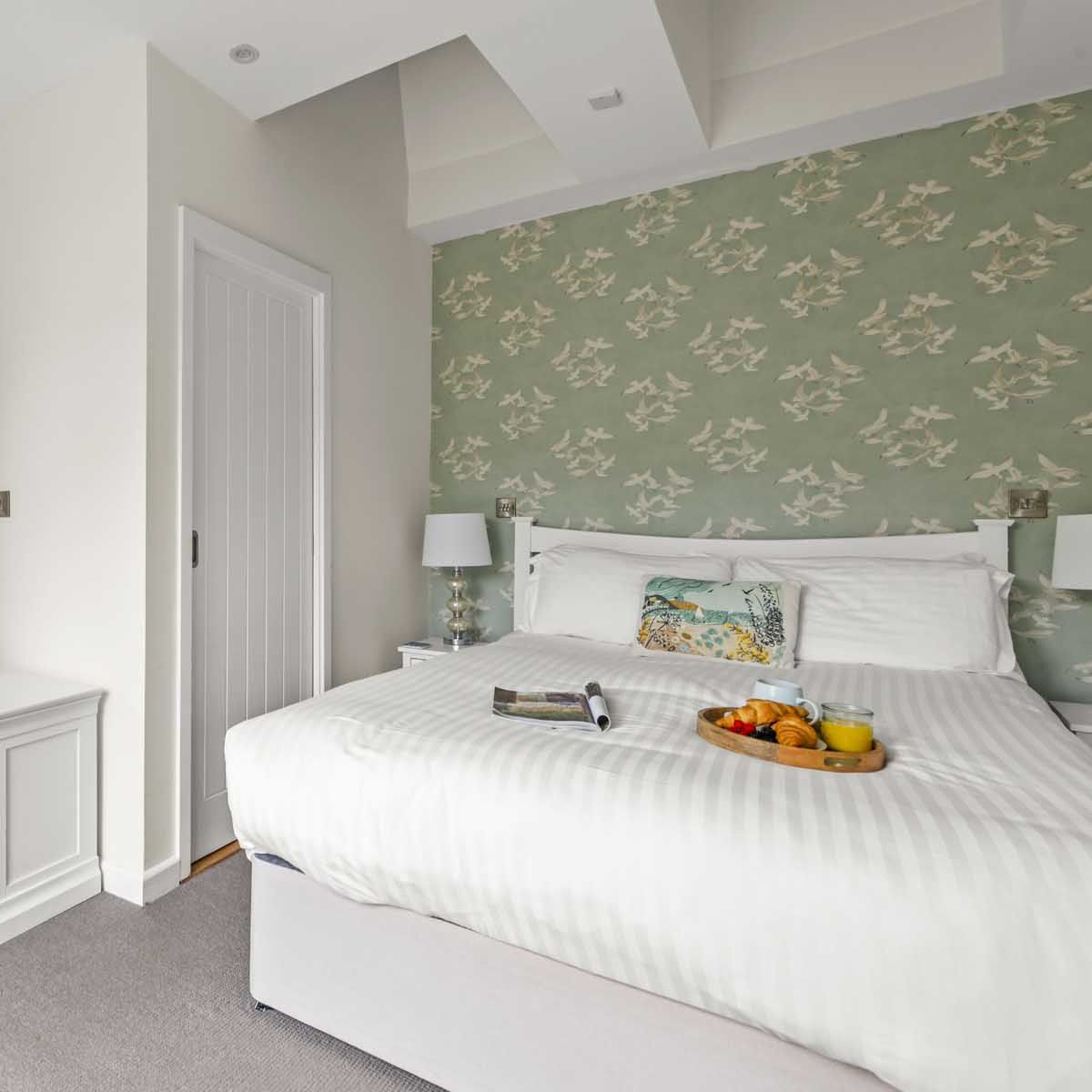 Modern bedroom with ensuite bathroom, white bed, and green floral wallpaper
