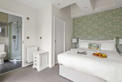 Modern bedroom with ensuite bathroom, white bed, and green floral wallpaper