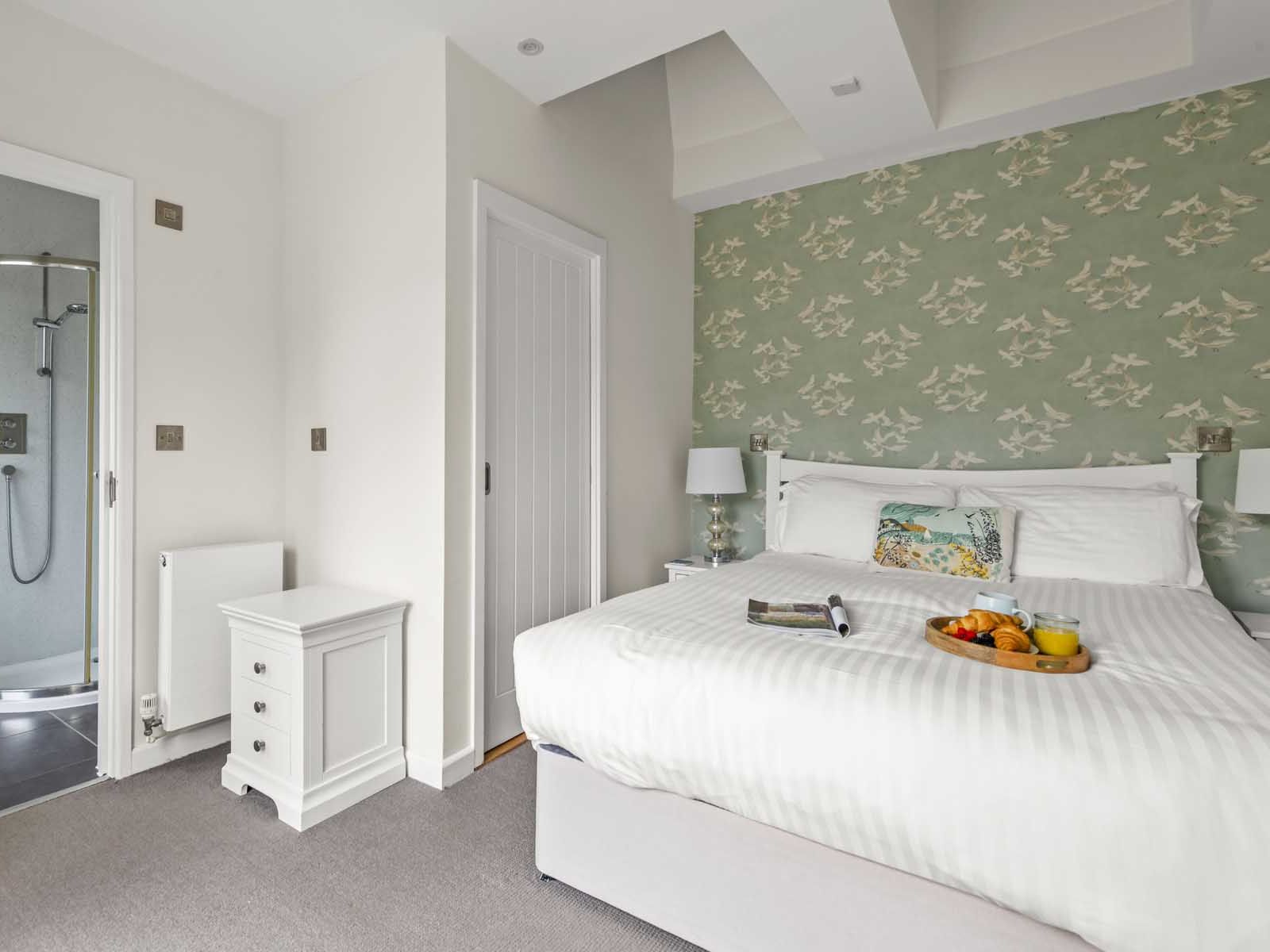 Modern bedroom with ensuite bathroom, white bed, and green floral wallpaper