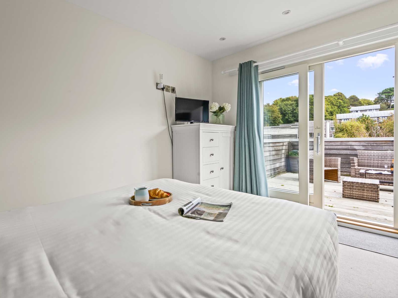 Bright bedroom with white bed, dresser, TV, and outdoor patio view