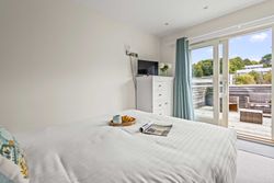Bright bedroom with white bed, dresser, TV, and outdoor patio view