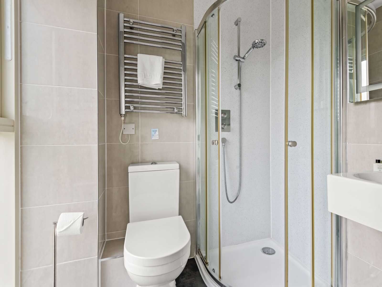 Modern bathroom with toilet, glass shower enclosure, towel rack, and sink