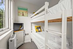 Small bedroom with white bunk beds, dog-themed pillow, wall art, and TV.