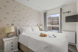 Bright bedroom with seagull wallpaper, white bed linens, tray with breakfast, and mounted TV.