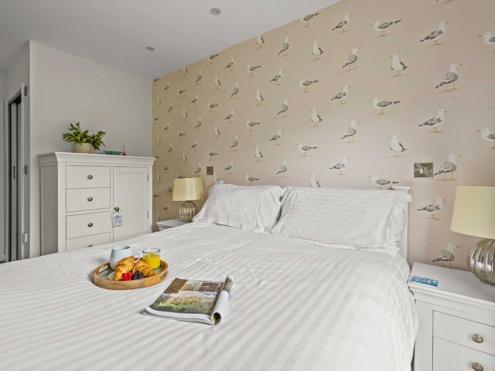 Cozy bedroom with white furniture, seagull wallpaper, and breakfast tray on the bed