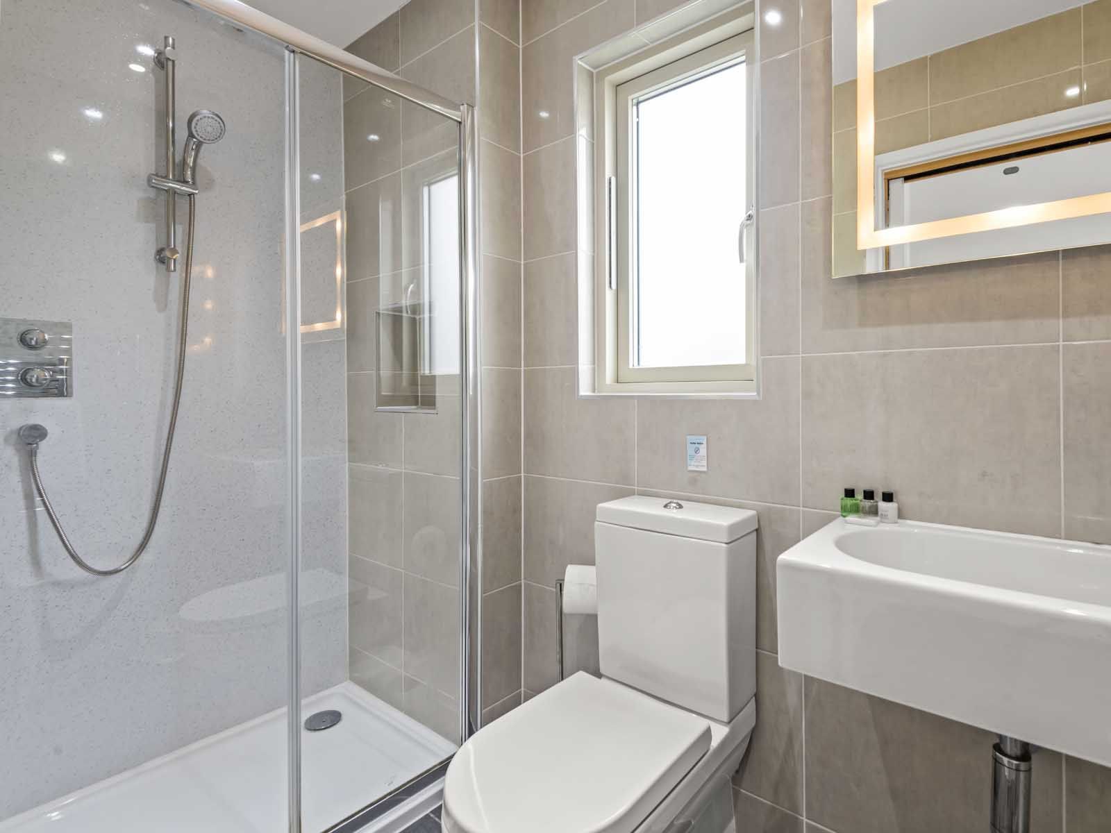 Modern bathroom with glass shower, toilet, sink, and illuminated mirror