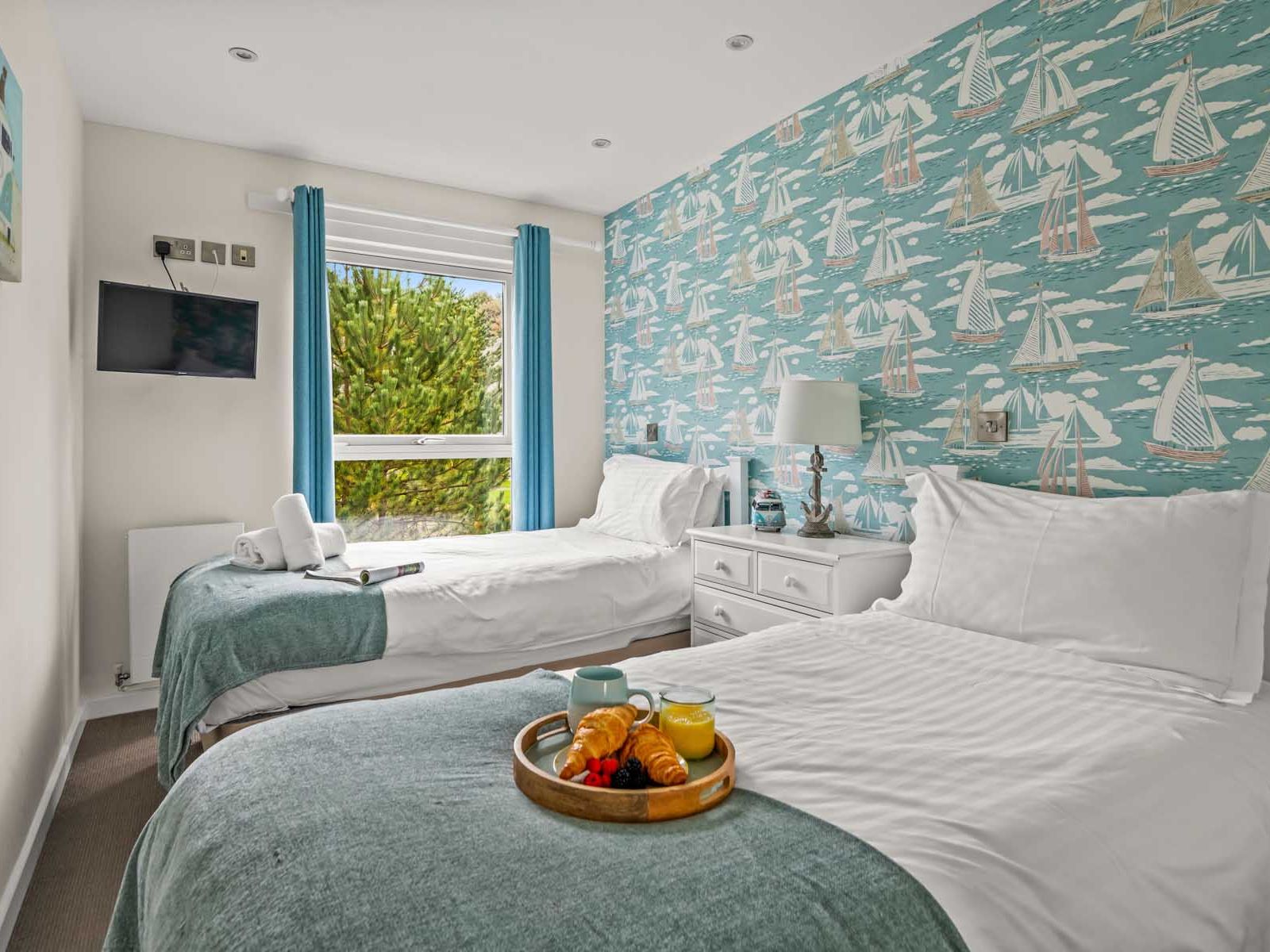 Twin bedroom with nautical wallpaper, breakfast tray, and window with blue curtains