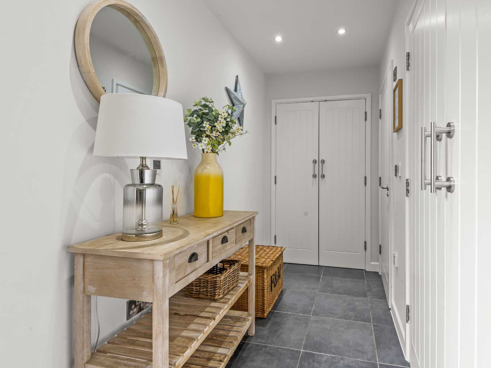 Modern hallway interior with wooden console table, decorative mirror, lamp, and yellow vase with flowers.