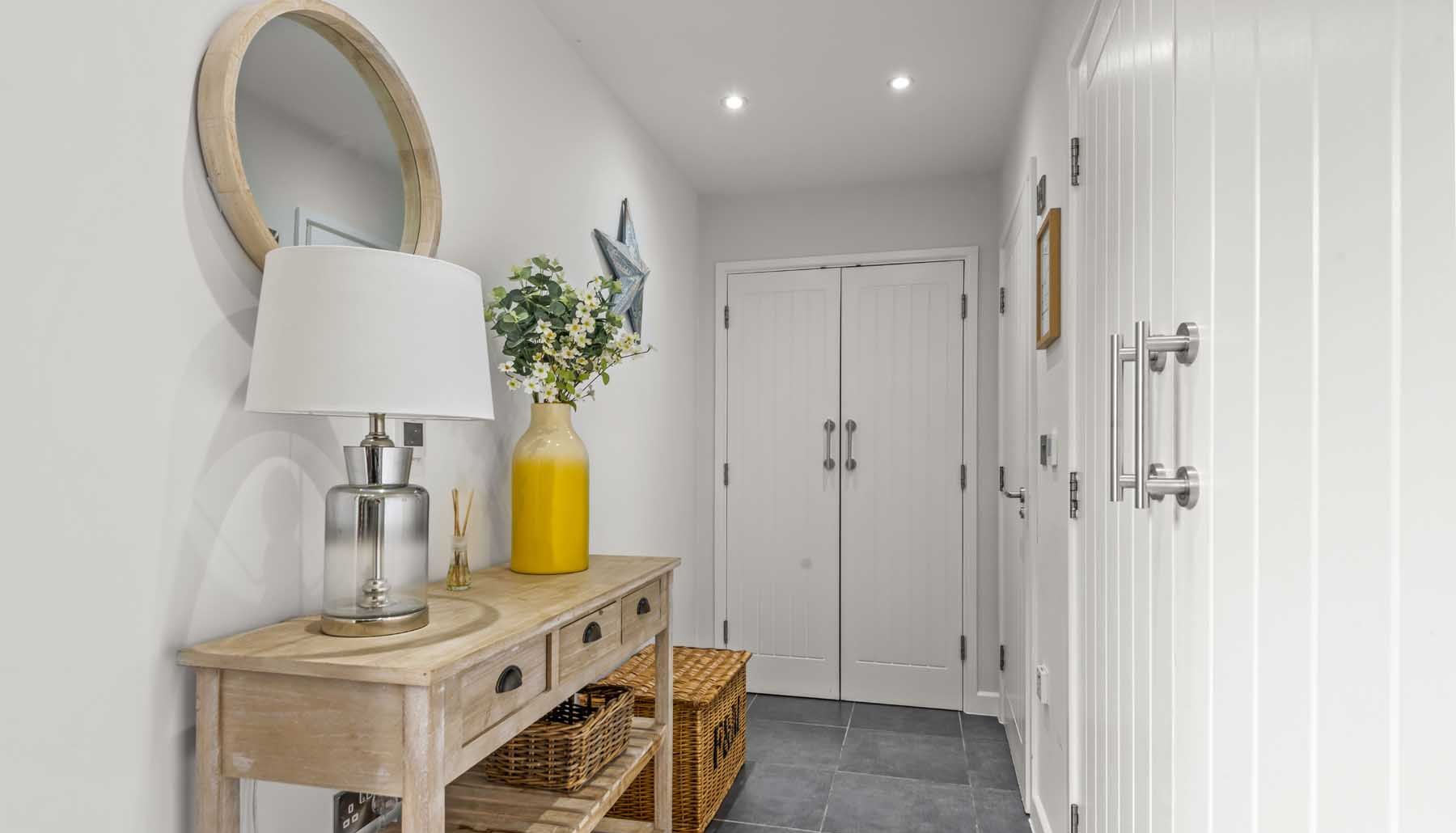 Modern hallway interior with wooden console table, decorative mirror, lamp, and yellow vase with flowers.