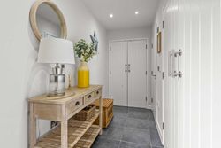 Modern hallway interior with wooden console table, decorative mirror, lamp, and yellow vase with flowers.