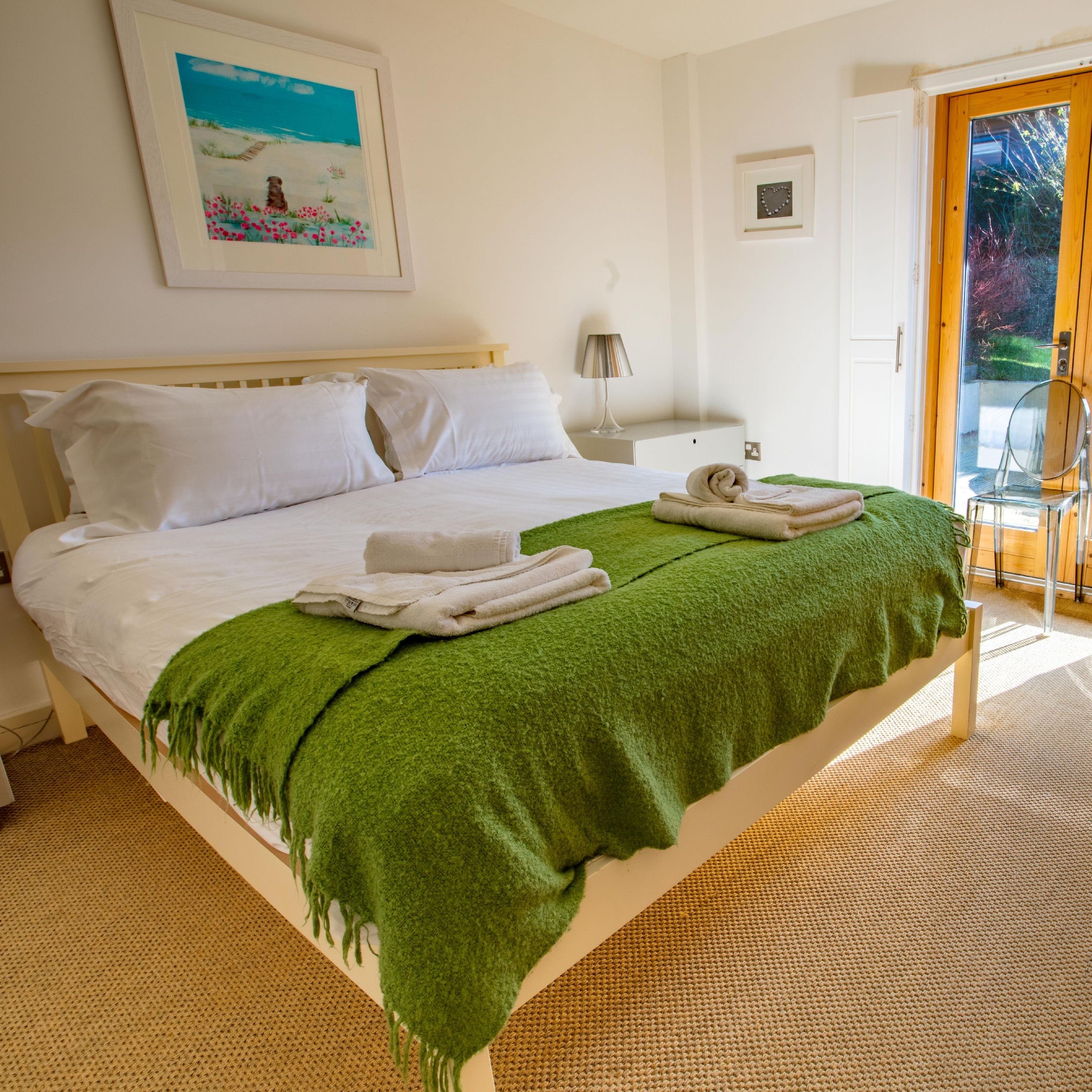 Bright bedroom with double bed, green blanket, and patio doors leading to a garden