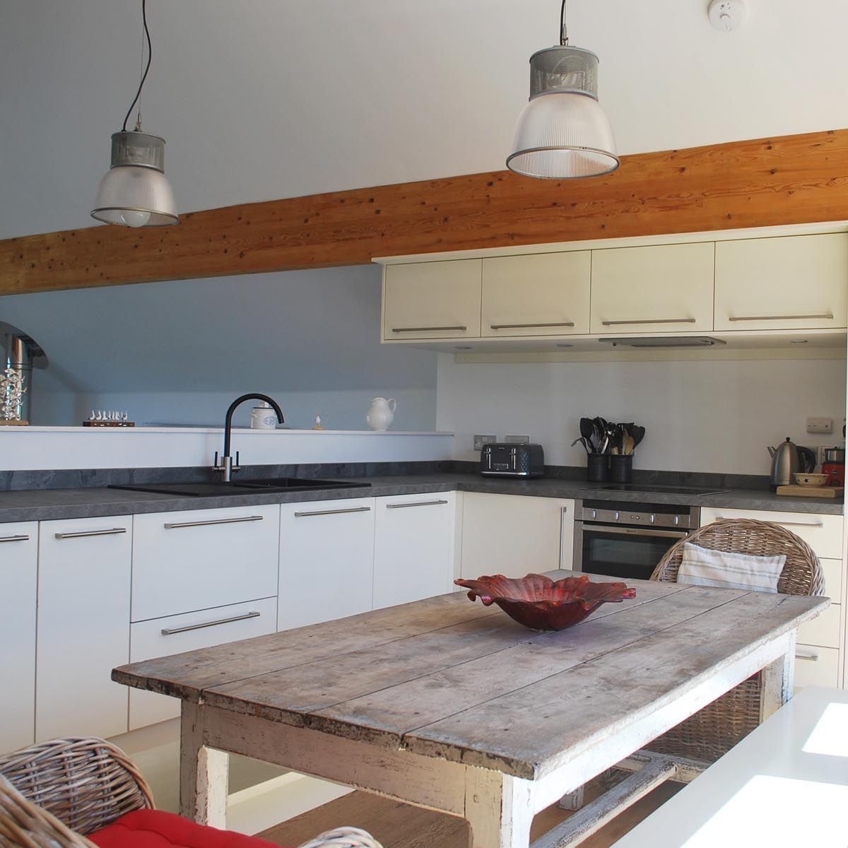 Modern kitchen with white cabinets, wooden beam, rustic table, and wicker chairs.