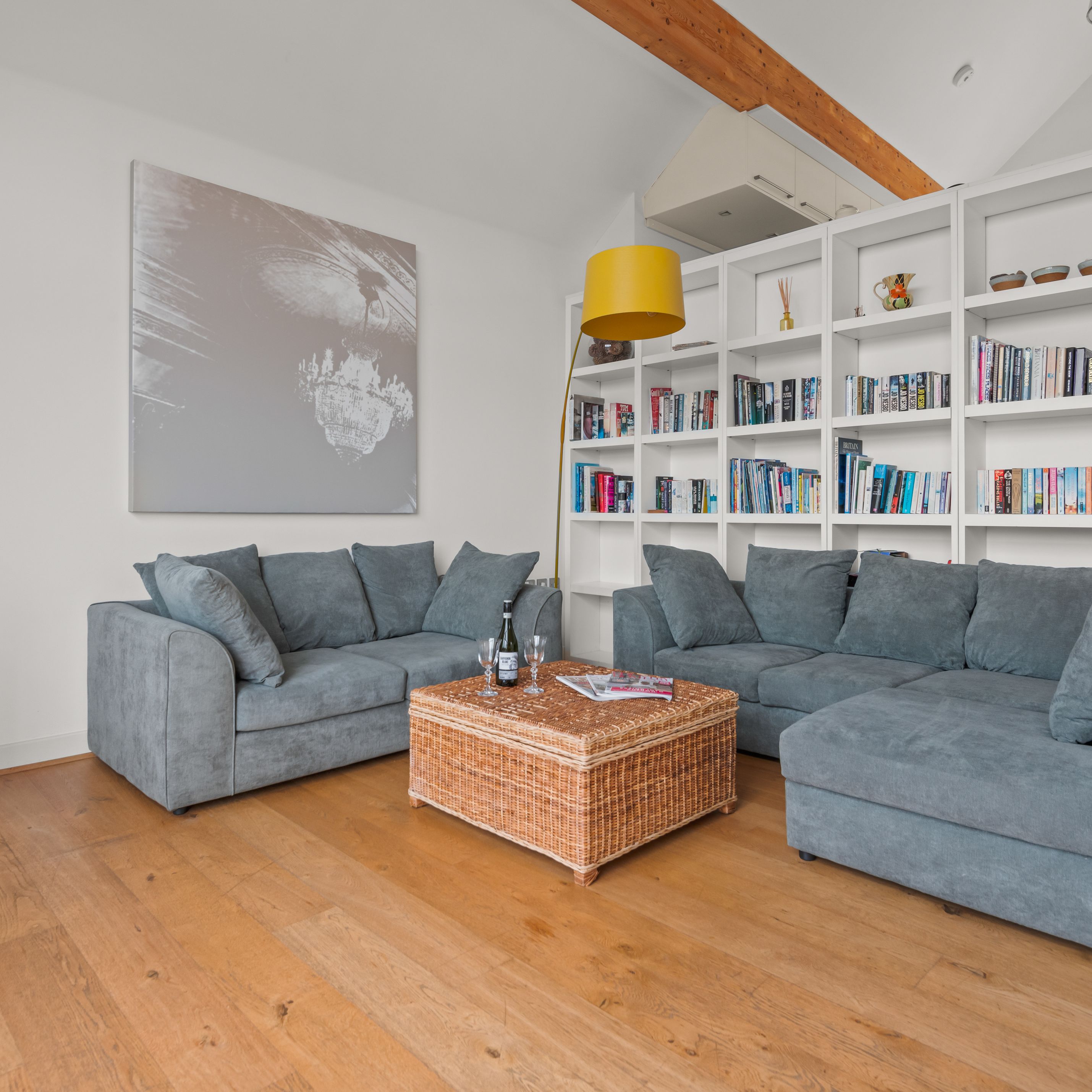 Modern living room with blue sofas, wood stove, wicker coffee table, bookshelf, and yellow lamp