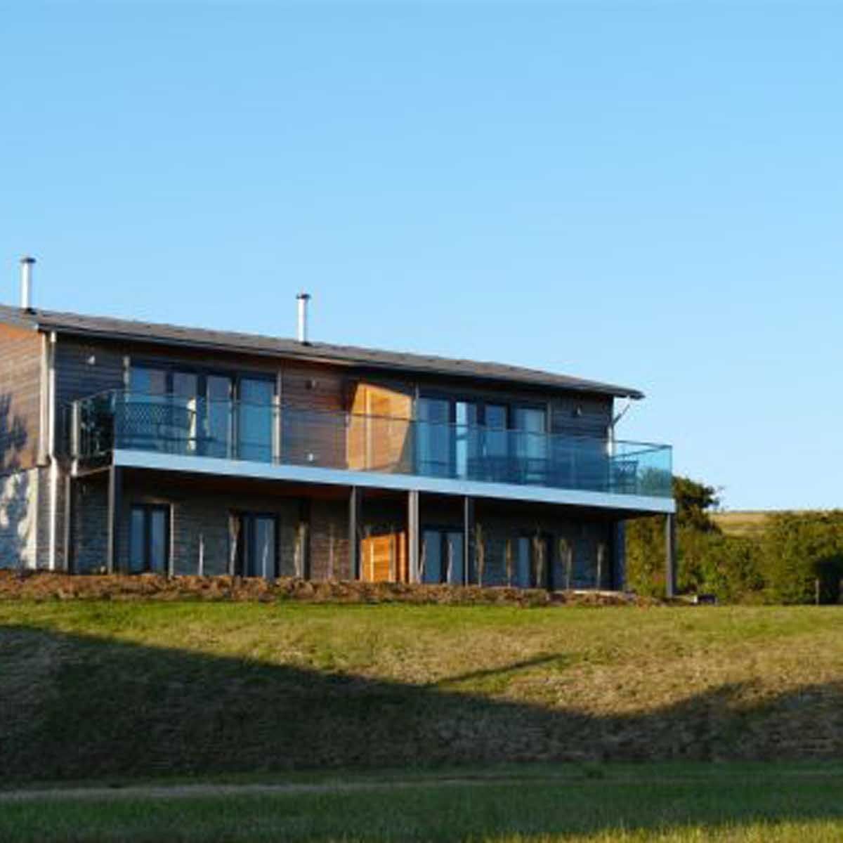 Modern two-story house with wood and stone exterior, large windows, and balcony.