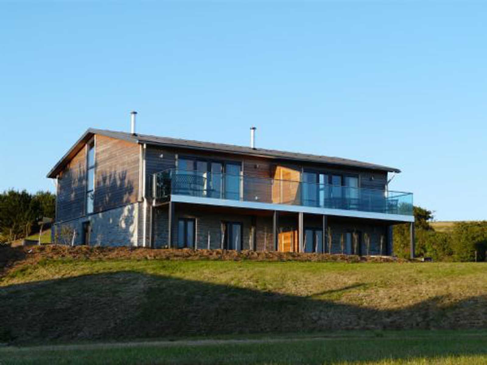Modern two-story house with wood and stone exterior, large windows, and balcony.