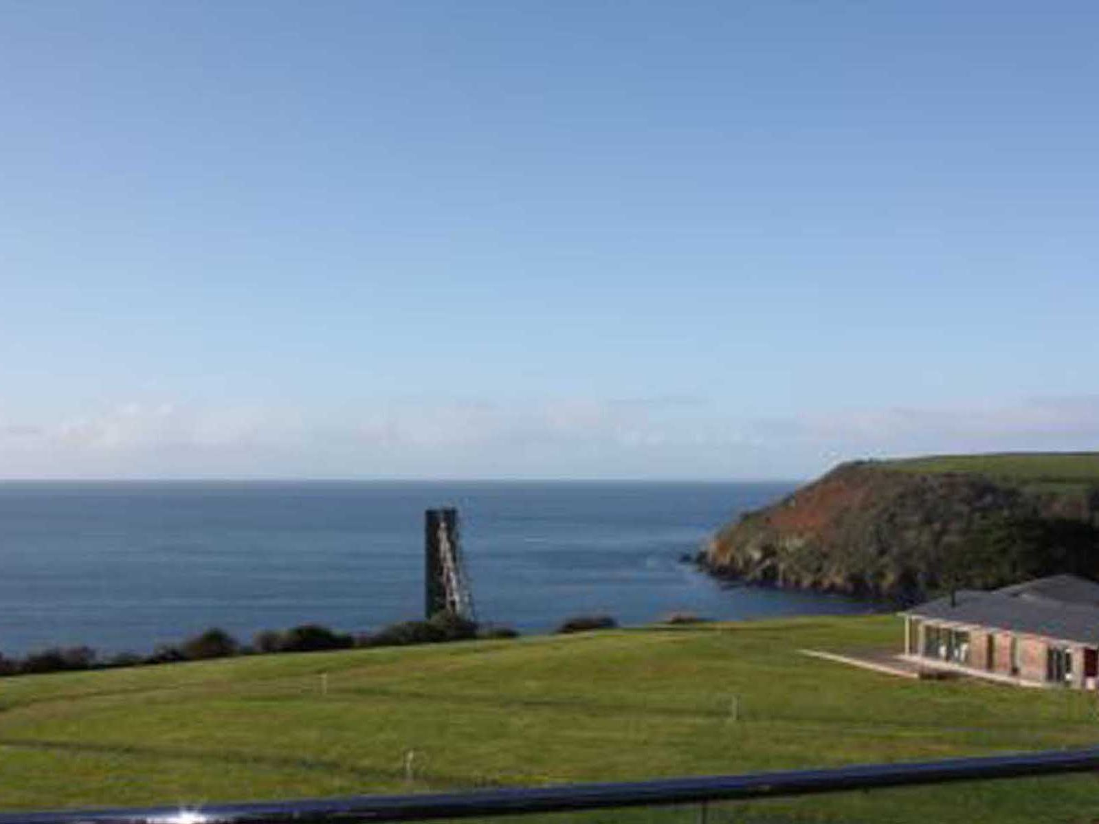Coastal landscape with a grassy field, an old stone tower near the sea, and a small building on the right