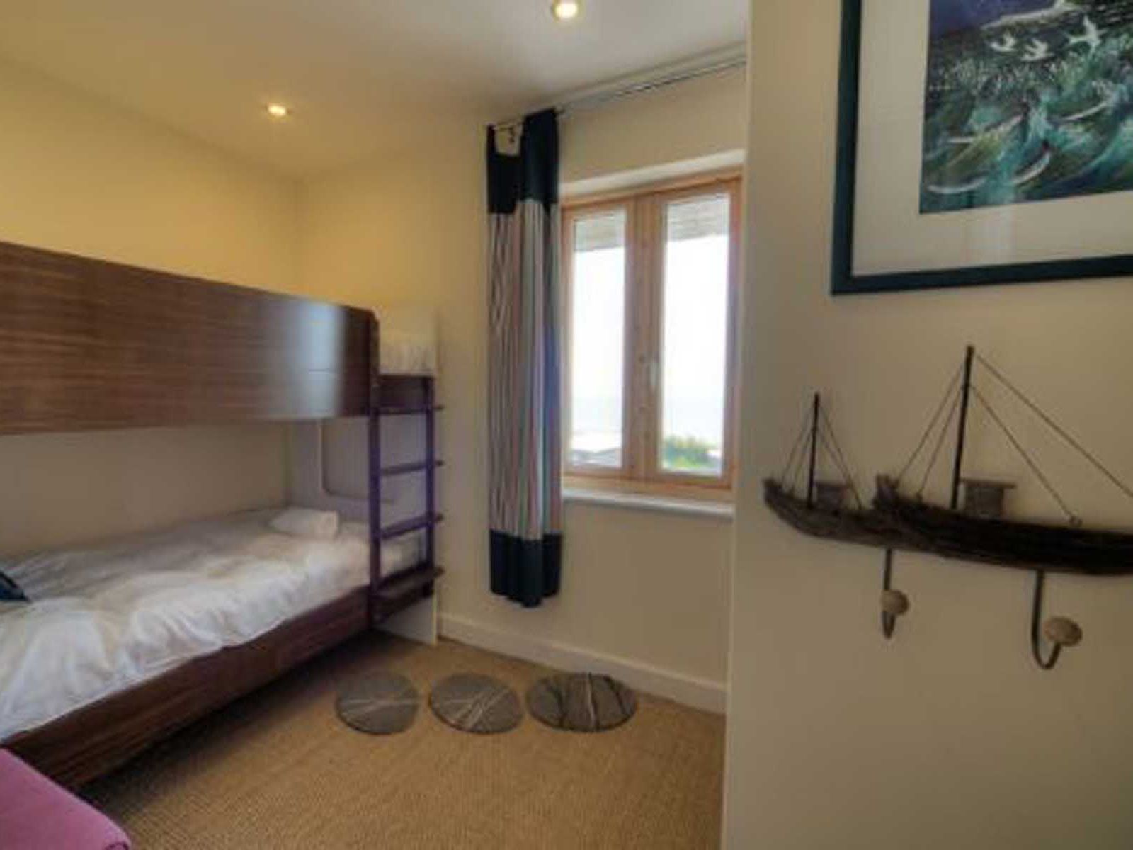 Small bedroom with wooden bunk beds, window, round rugs, and nautical decorations on the wall