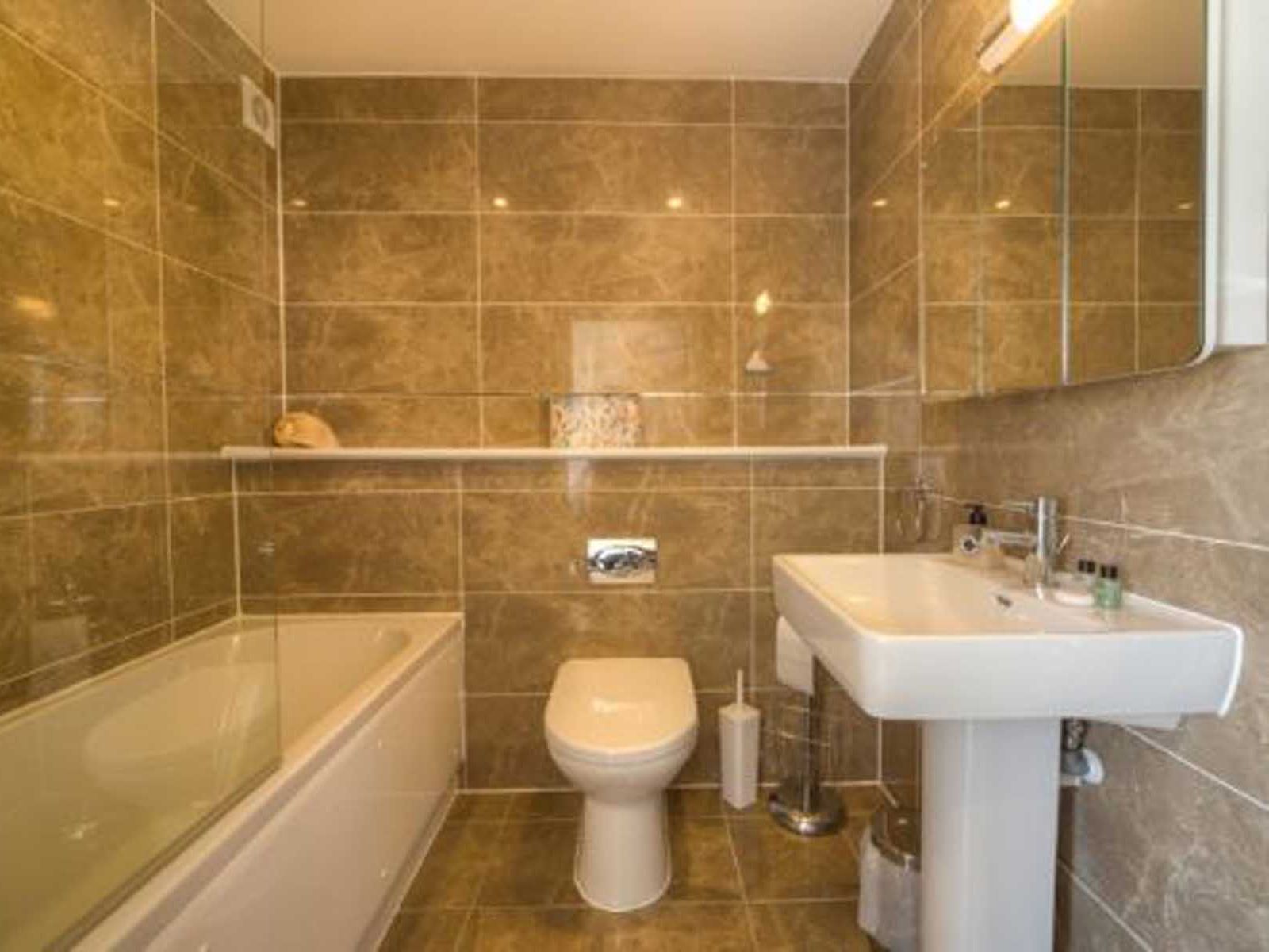Modern bathroom with brown tiles, bathtub, toilet, and sink