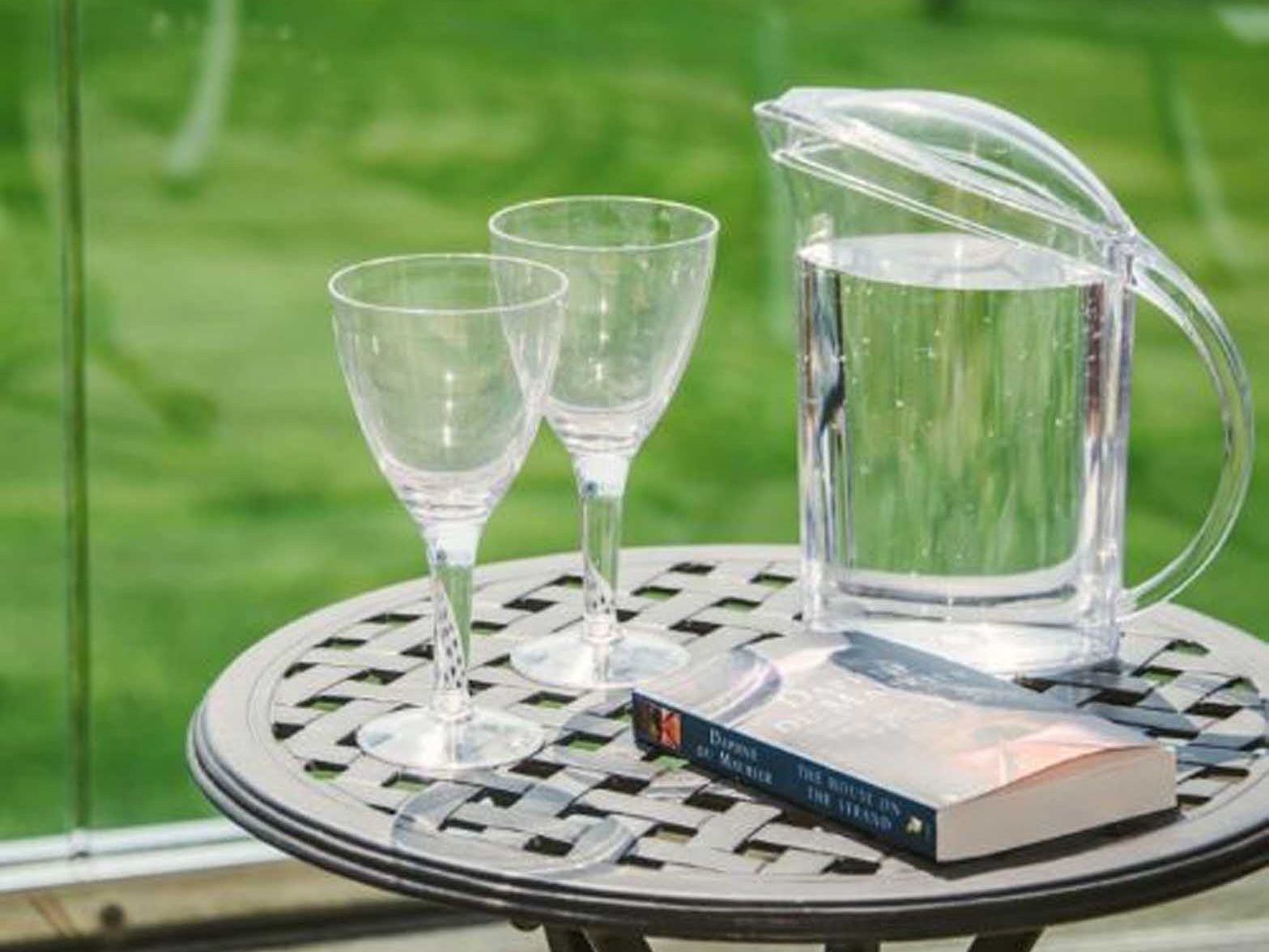 Two empty wine glasses, a clear jug of water, and a book on a round outdoor metal table
