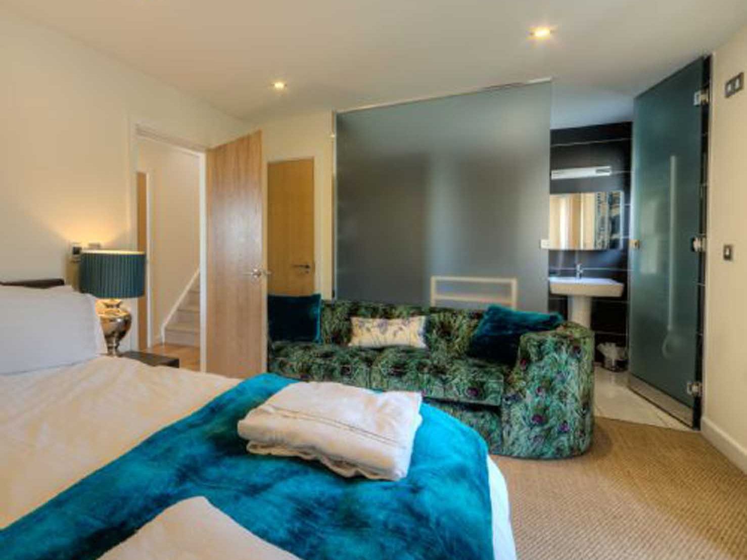 Modern bedroom with a green patterned sofa, blue accents, and an ensuite bathroom with frosted glass doors.