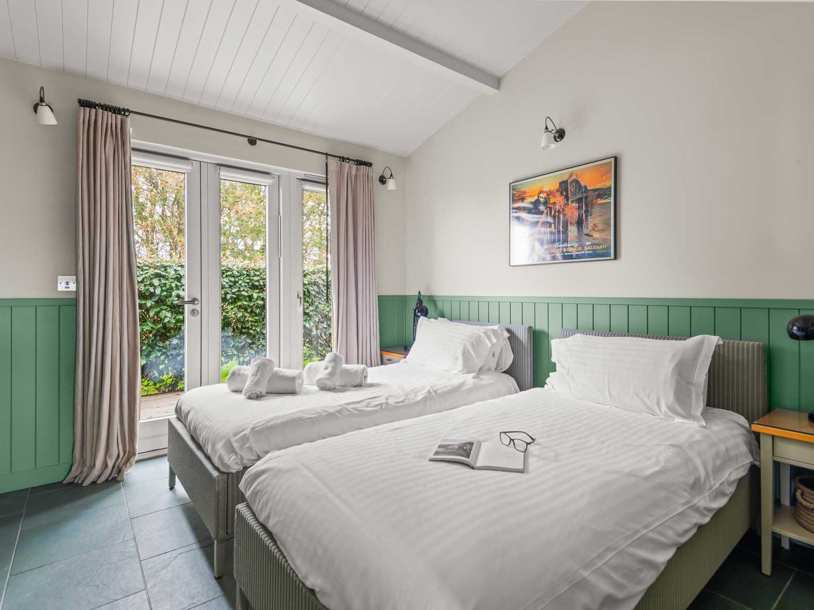 Bright bedroom with twin beds, green wainscoting, and French doors leading outside.