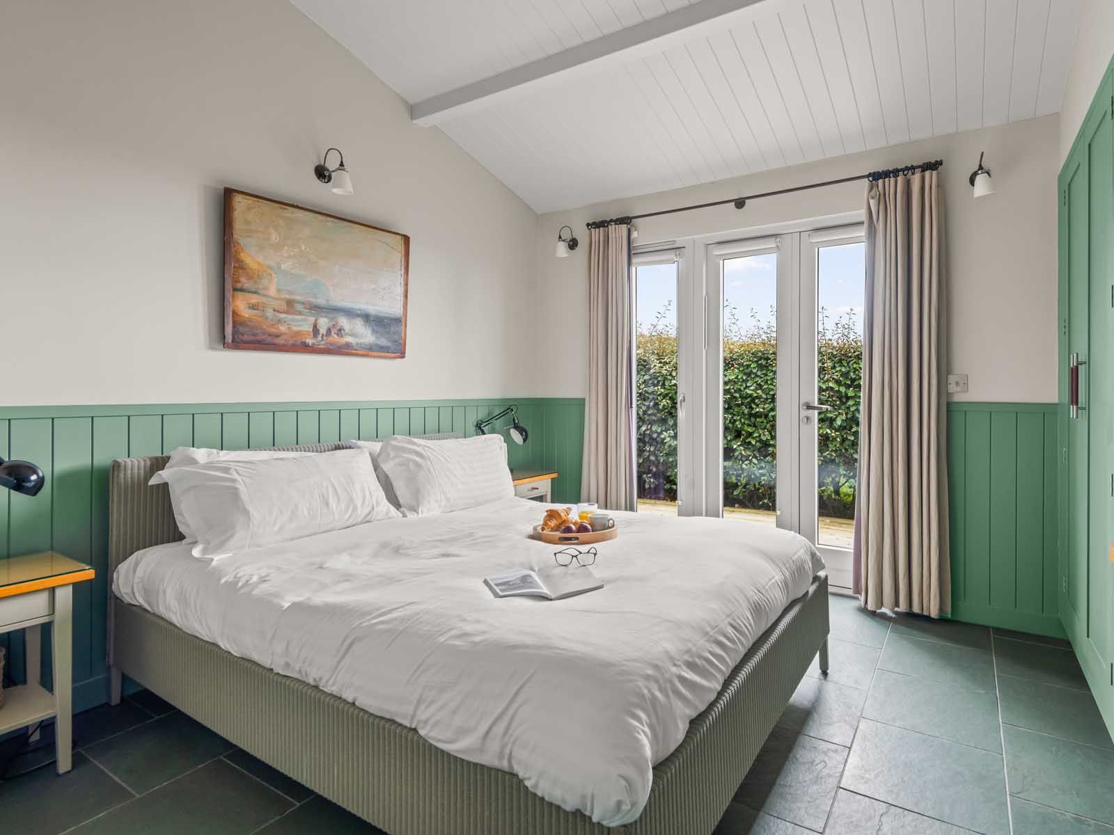 Cozy bedroom with green accents, large bed, and French doors opening to a garden.