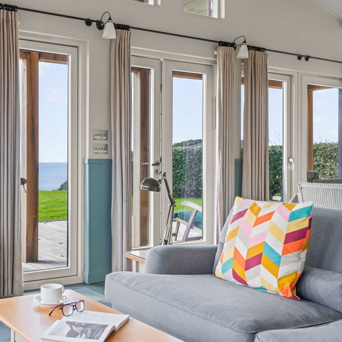 Cozy living room with wood burning stove, colorful cushion, and large windows overlooking the ocean.