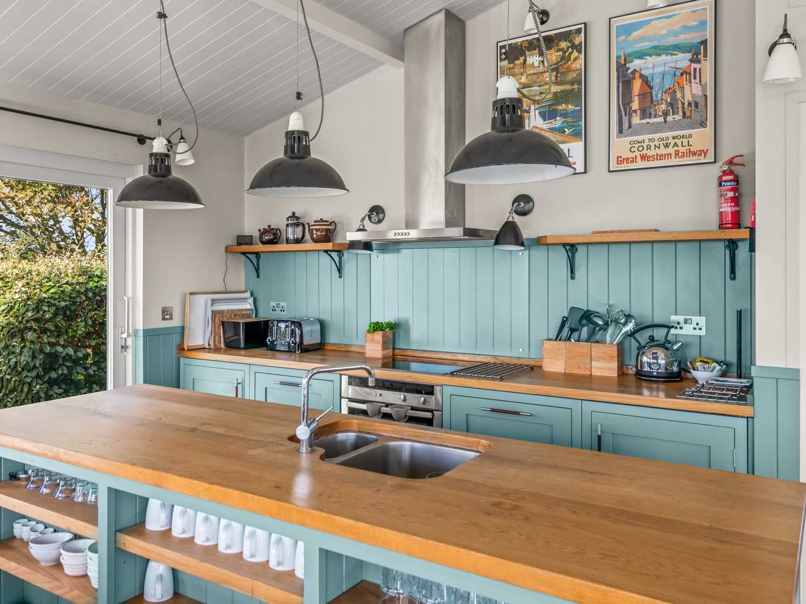 Modern country kitchen with teal cabinets, wooden countertops, and large pendant lights.