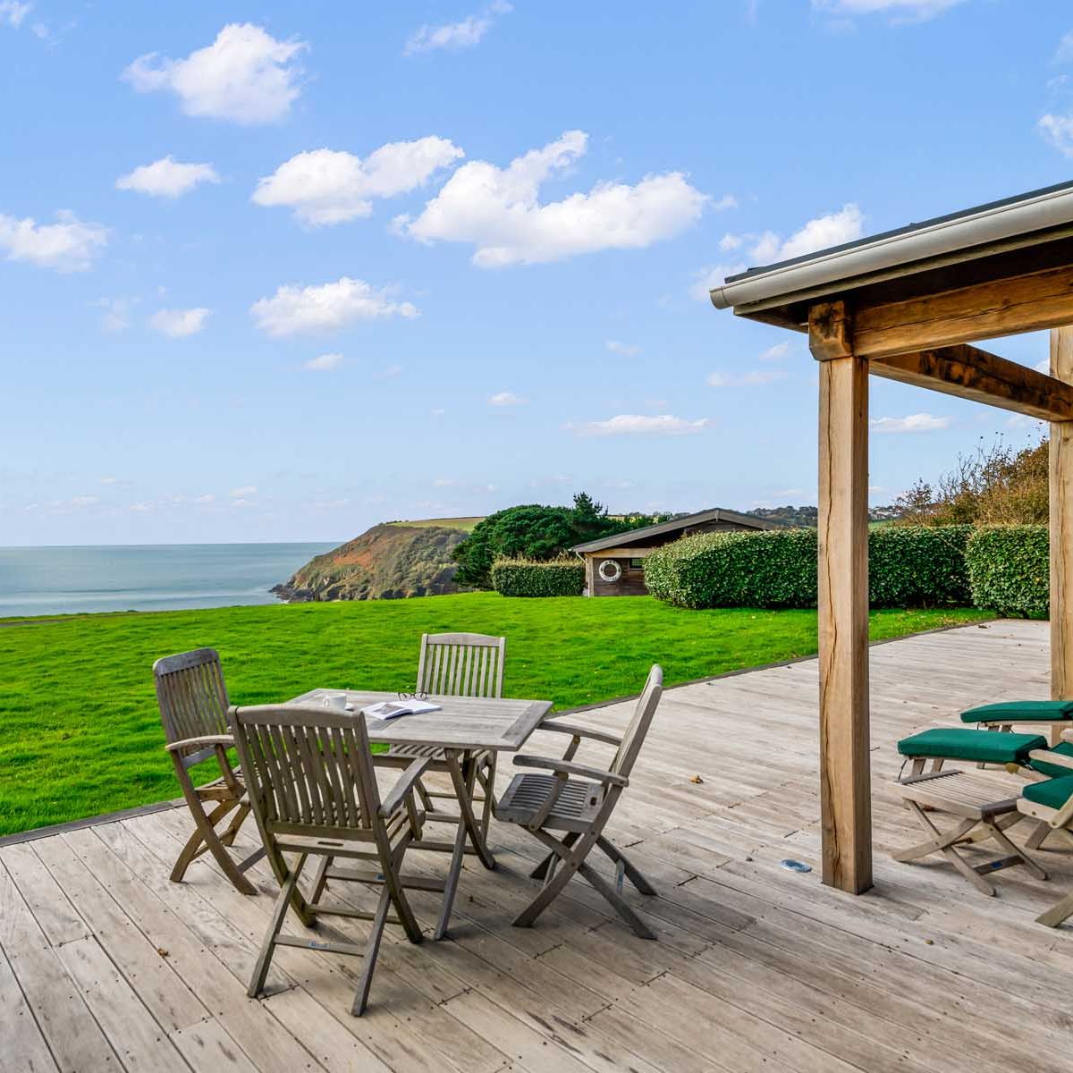 Wooden deck with outdoor furniture overlooking grassy yard and ocean view