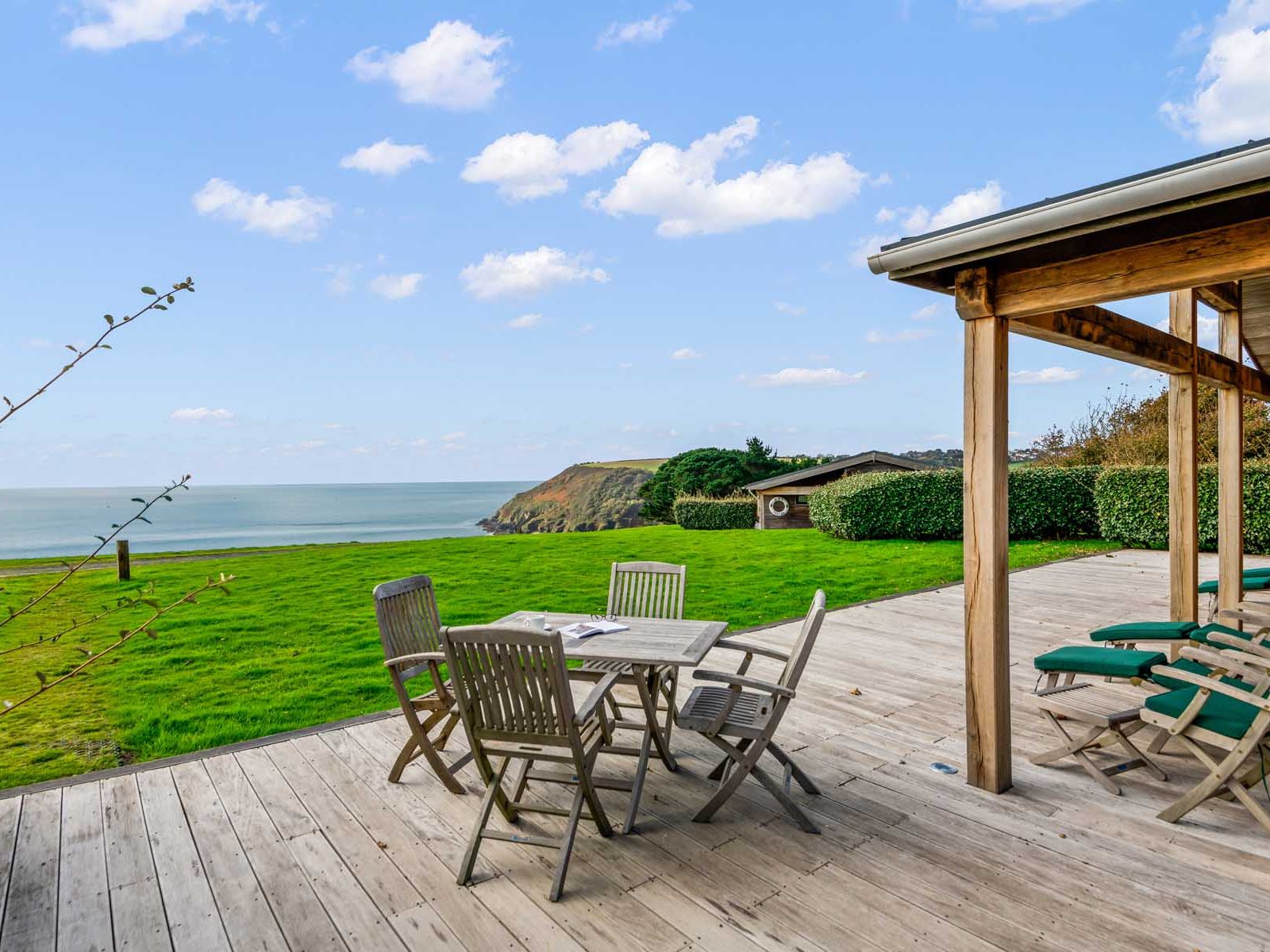 Wooden deck with outdoor furniture overlooking grassy yard and ocean view