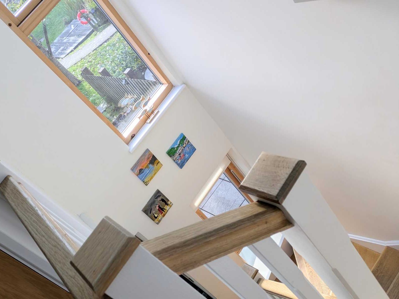 Staircase with wooden railing, white walls, and window overlooking a garden with paintings on the wall.