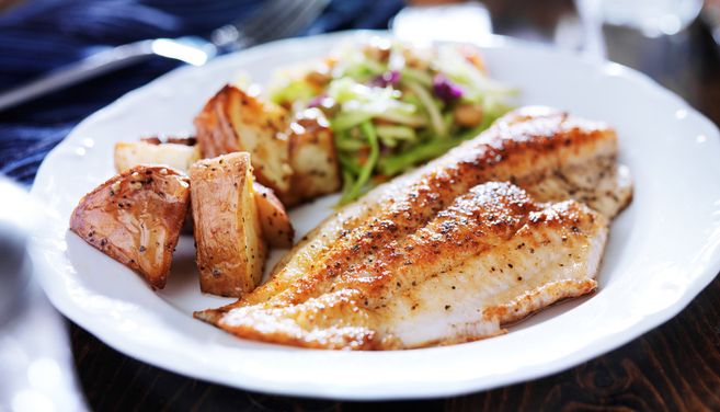 Grilled fish fillet served with roasted potatoes and vegetables on a white plate
