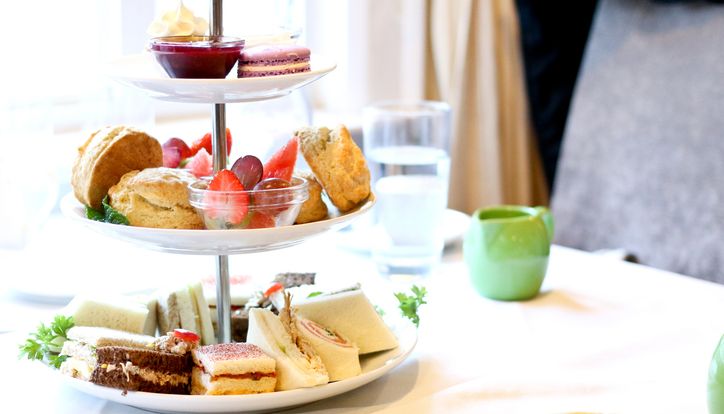 Three-tiered afternoon tea stand with assorted sandwiches, scones, desserts, and pastries on a white tablecloth.