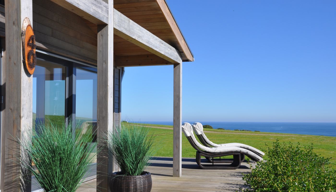 Modern wooden patio with lounge chairs overlooking a grassy lawn and the ocean