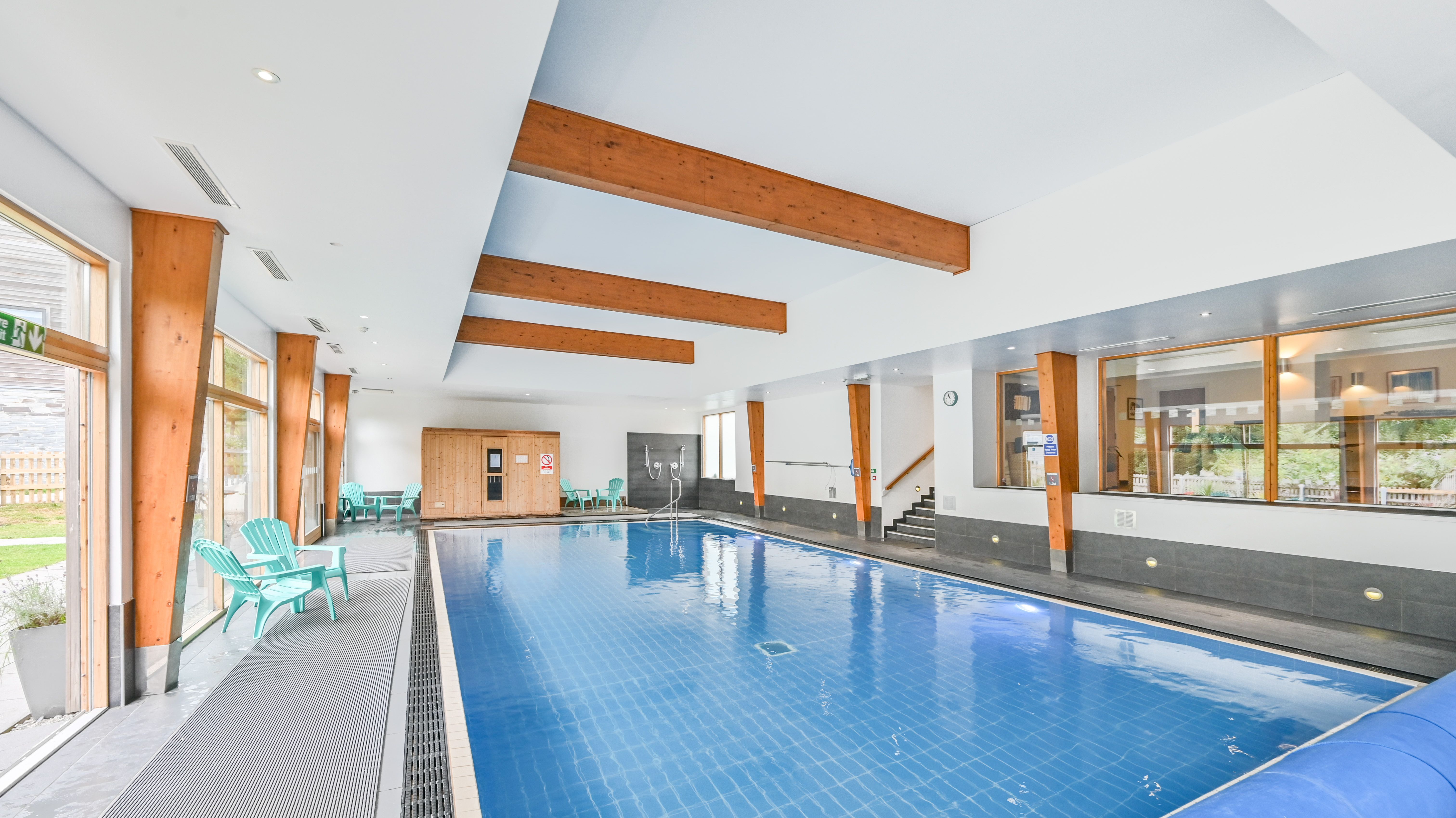 Modern indoor swimming pool with wood beams and lounge chairs