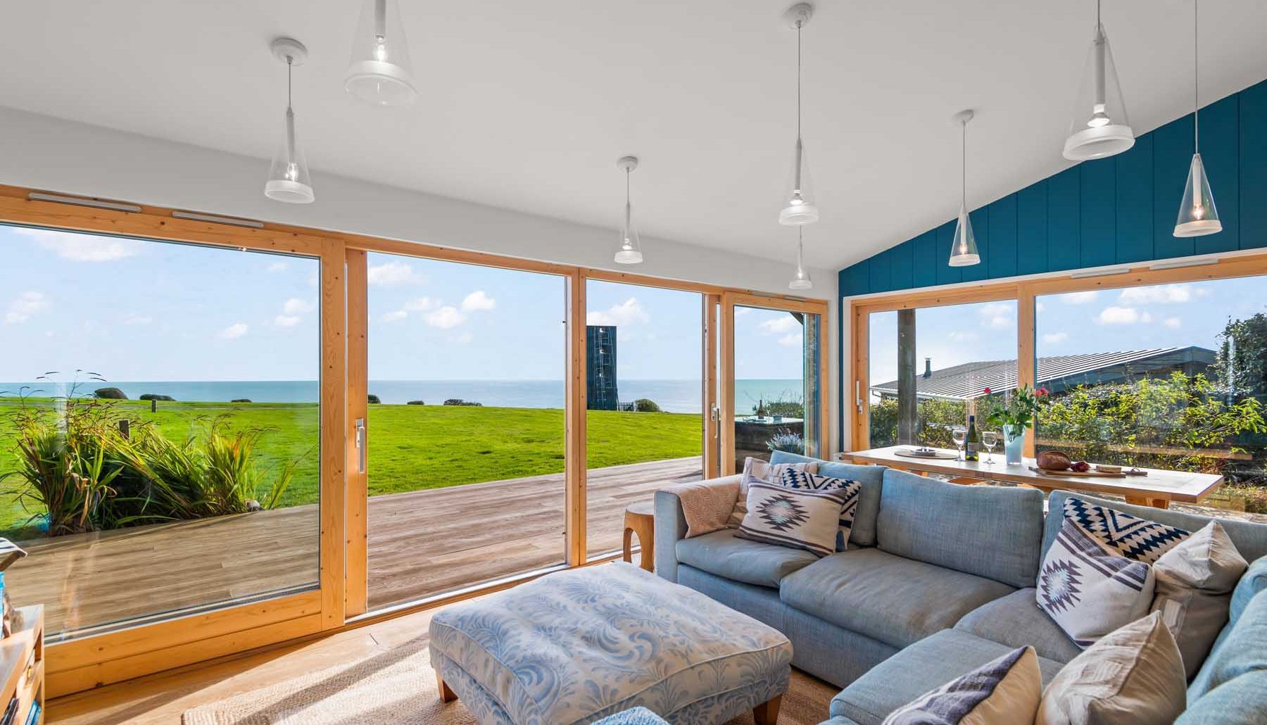 Modern living room with large windows overlooking a grassy yard and ocean view.