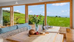 Modern dining area with large windows overlooking a green lawn and distant sea view
