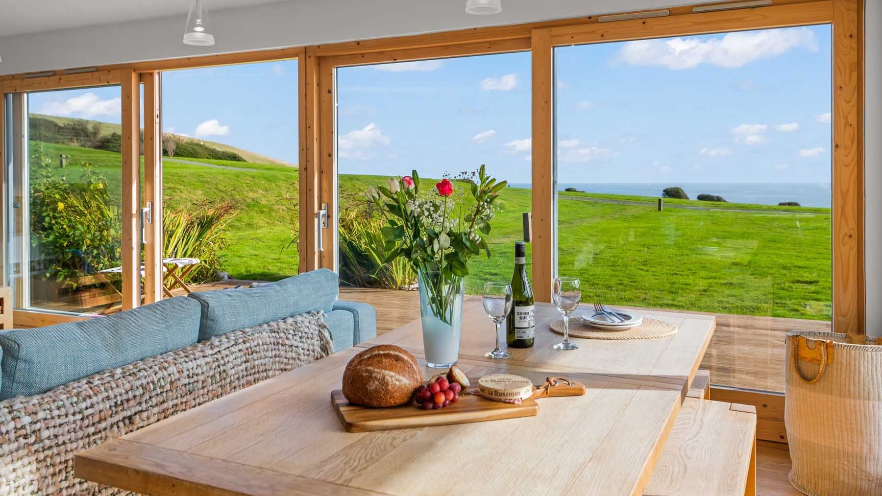 Modern dining area with large windows overlooking a green lawn and distant sea view