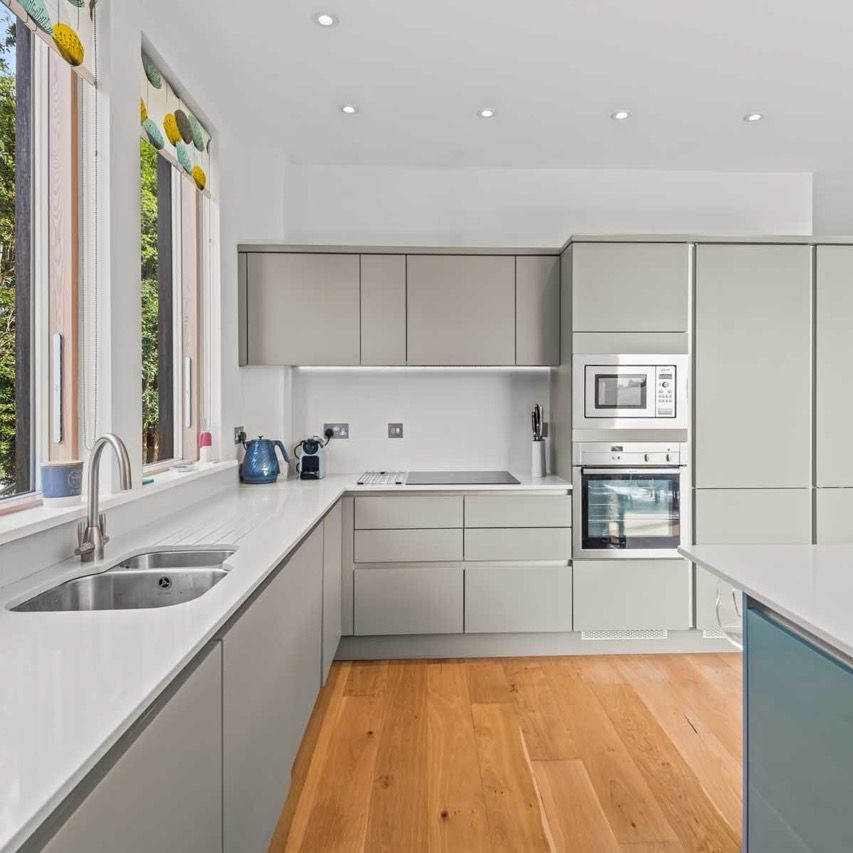 Modern kitchen with minimalist cabinets, white countertops, and wooden flooring.