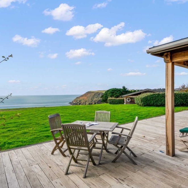 Wooden deck with outdoor seating overlooking a grassy lawn and the ocean.