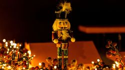 A wooden nutcracker figurine with a black hat and drum, surrounded by festive lights and decorations.