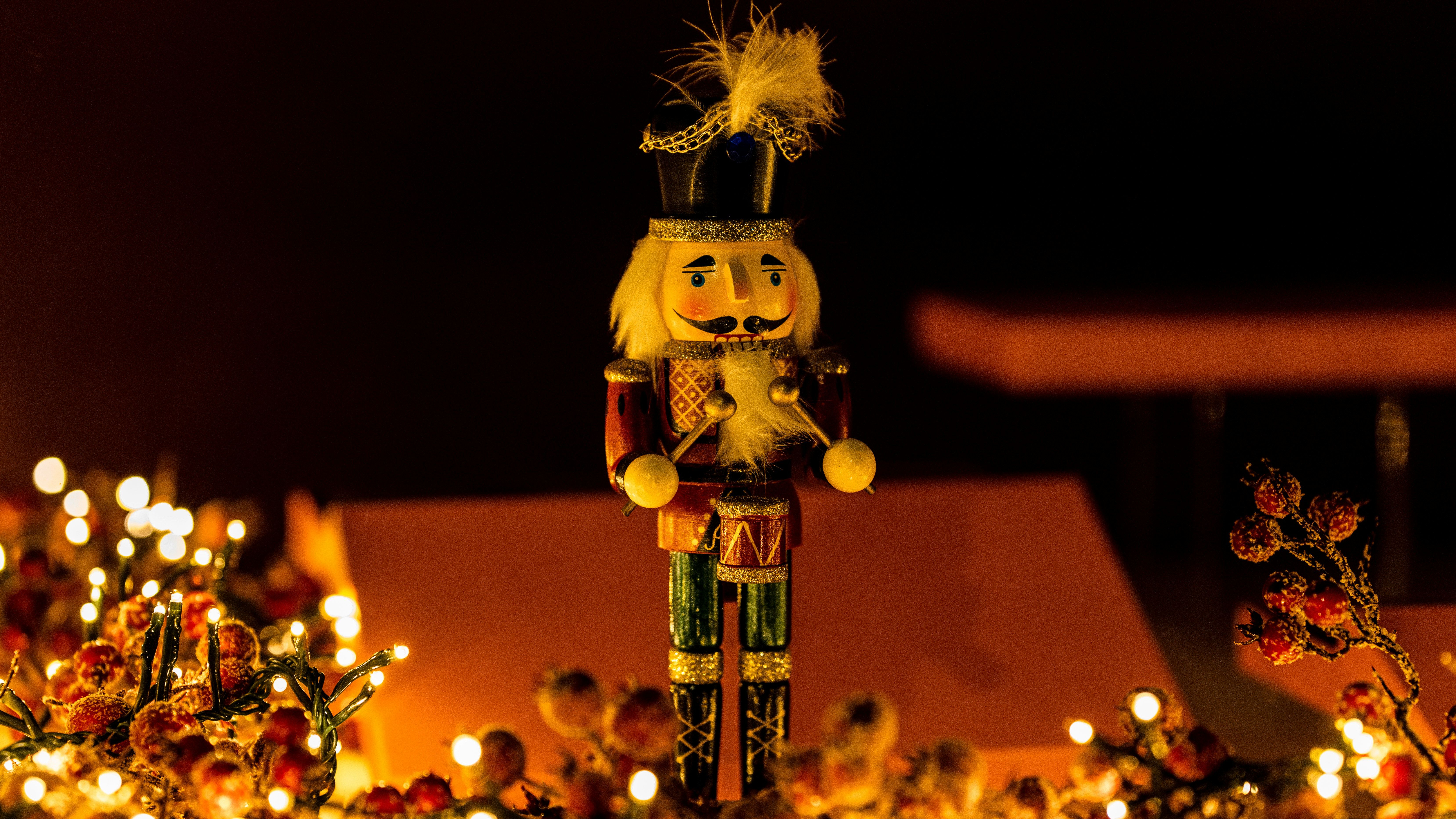 A wooden nutcracker figurine with a black hat and drum, surrounded by festive lights and decorations.