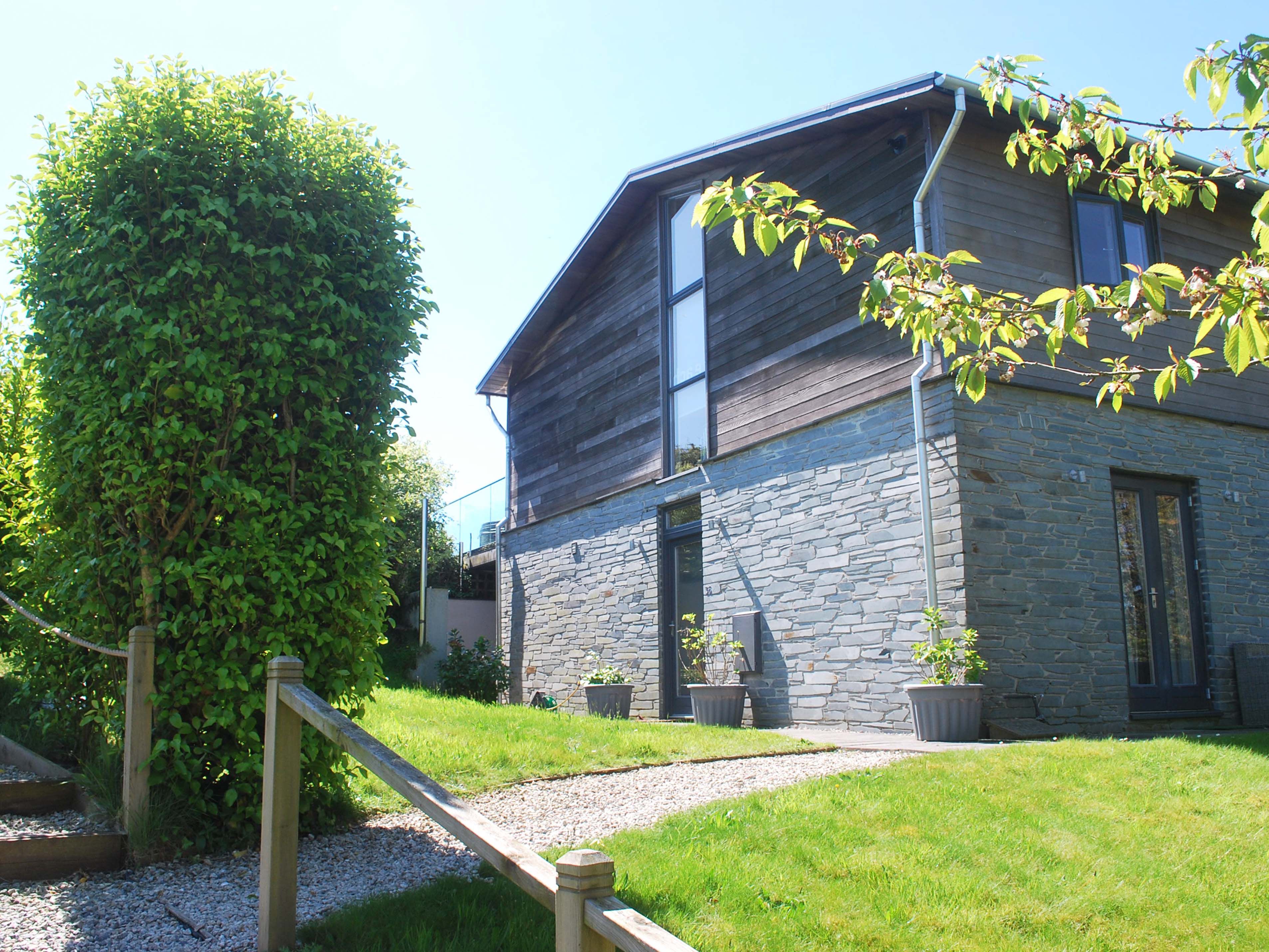 Modern house with stone and wood exterior, garden path, and lush greenery