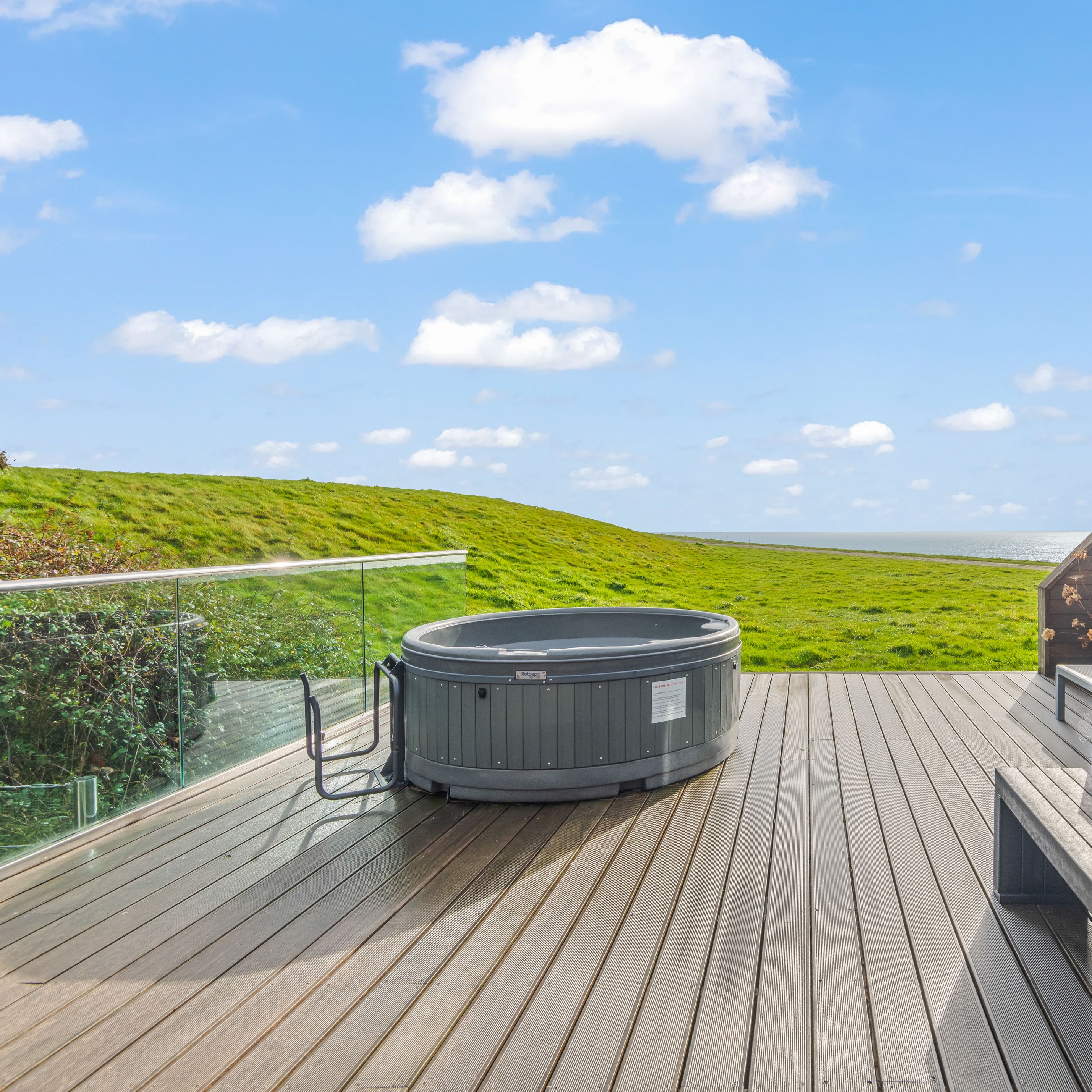 Outdoor deck with hot tub, picnic table, and scenic view of grassy hills and blue sky