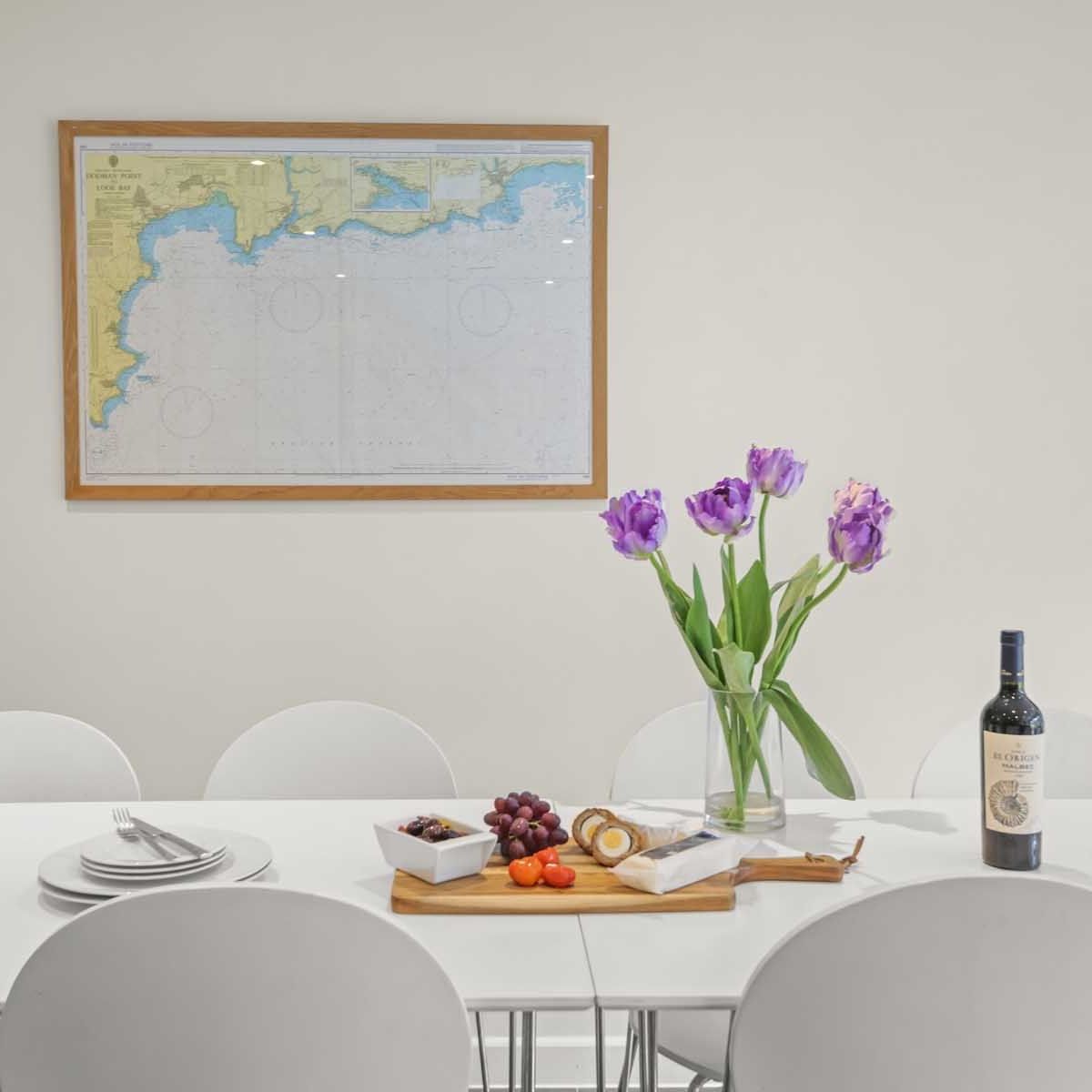 Modern dining table set with cheese, fruit, wine, purple flowers, and a map on the wall