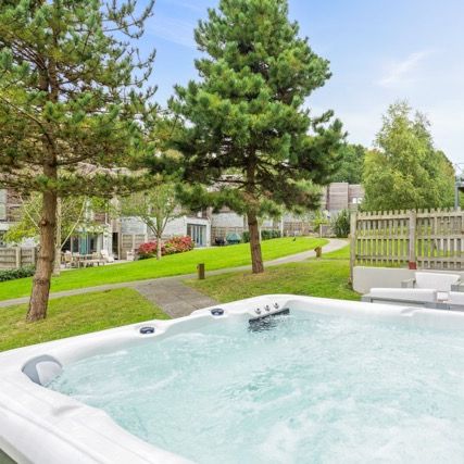 Outdoor hot tub with bubbling water in a modern landscaped garden with trees and contemporary buildings in the background.